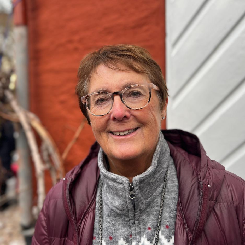 Aldrende kvinne med brunt kort h&aring;r, svarte og beige briller, som smiler. 