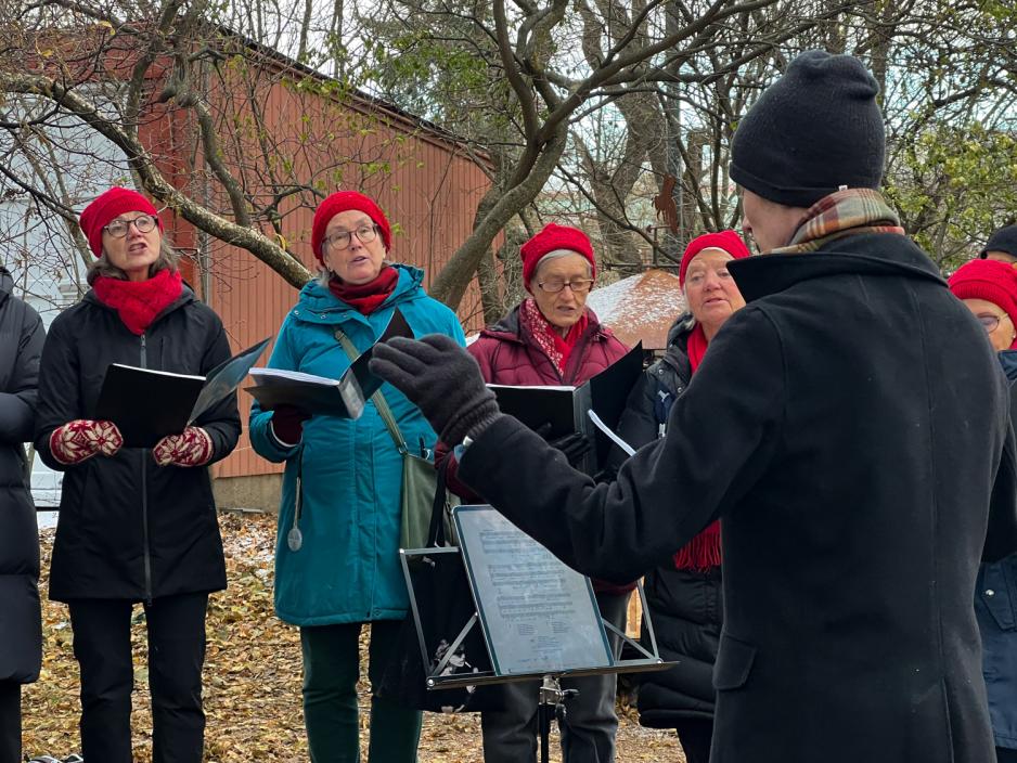 Kor som best&aring;r av flere aldrende kvinner, med dirigent til h&oslash;yre med henda i luften.