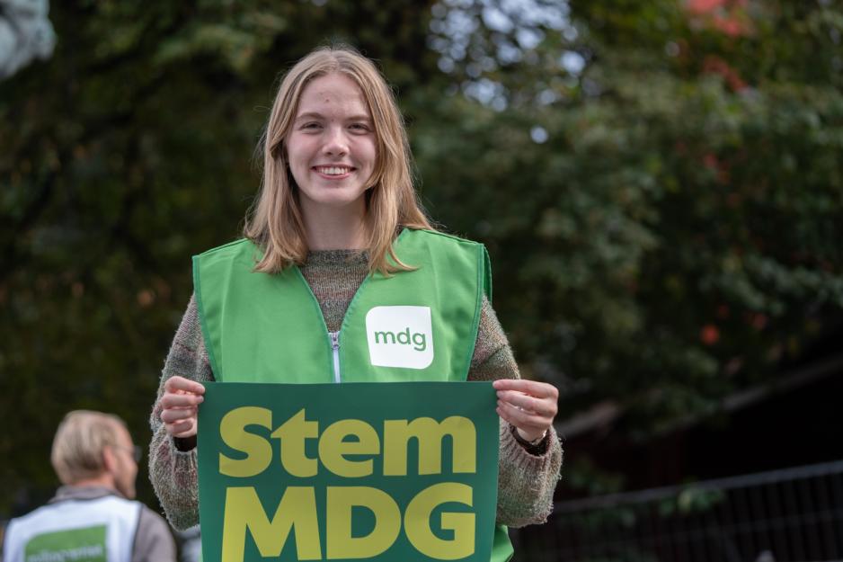 En jente i MDG vest, holder ett skilt med "Stem MDG"