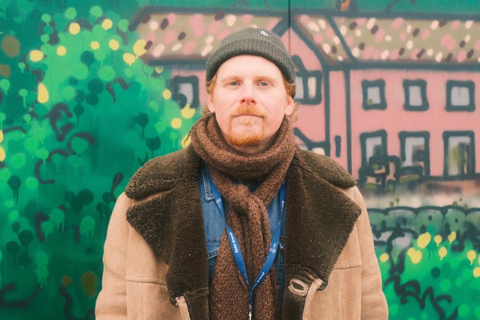 Mann med skjerf, lue og kåpe foran et veggmaleri