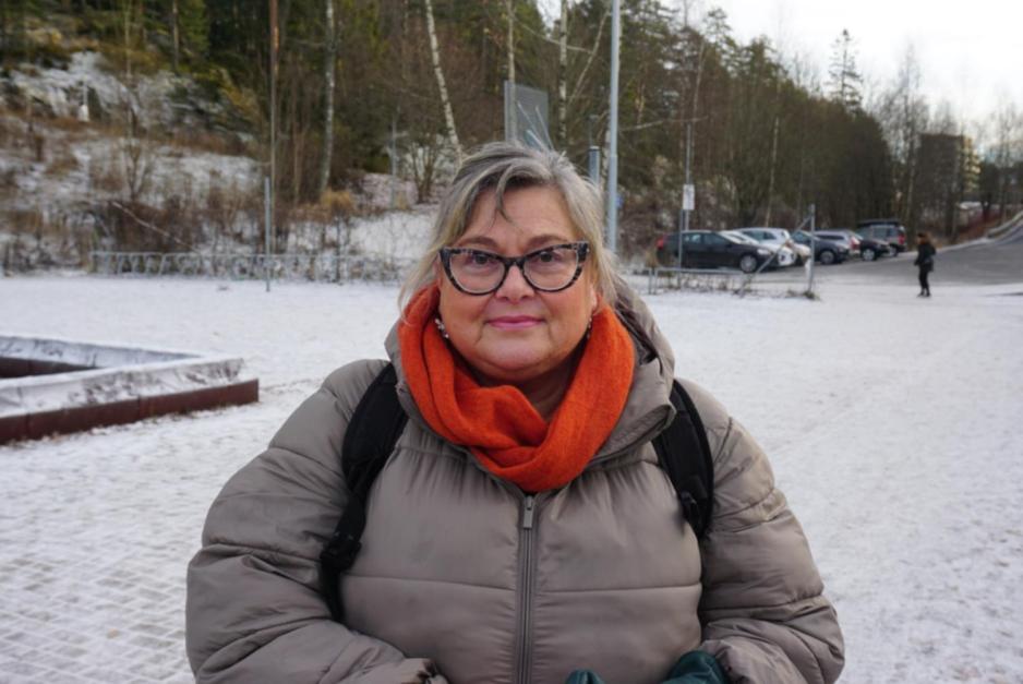 Kvinne i 60årene står godt kledd ute på vinteren. Snøen ligger på bakken rundt henne