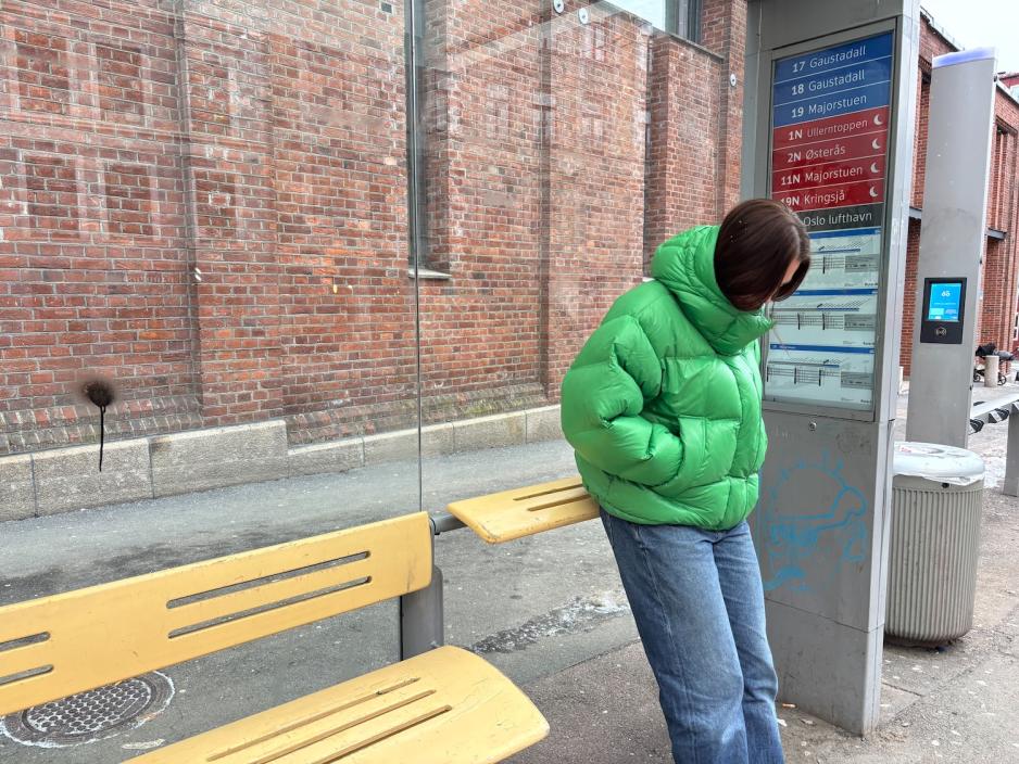 jente som lener seg på en skeiv benk på trikkestoppet Frydenlund i Oslo