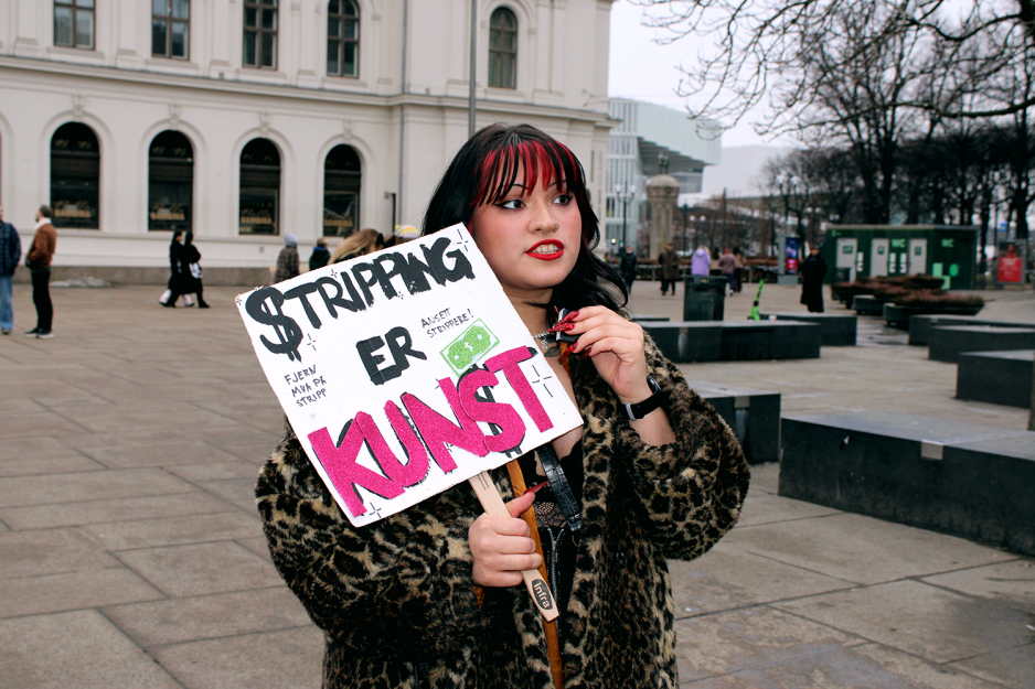 Stripper Alma Adoreholder en plakat der det står "Stripping er Kunst"