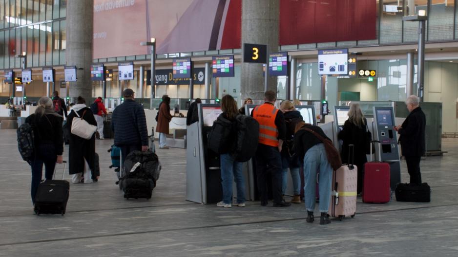 Lufthavnpresten hjelper en passasjer å printe ut bagasjelapp