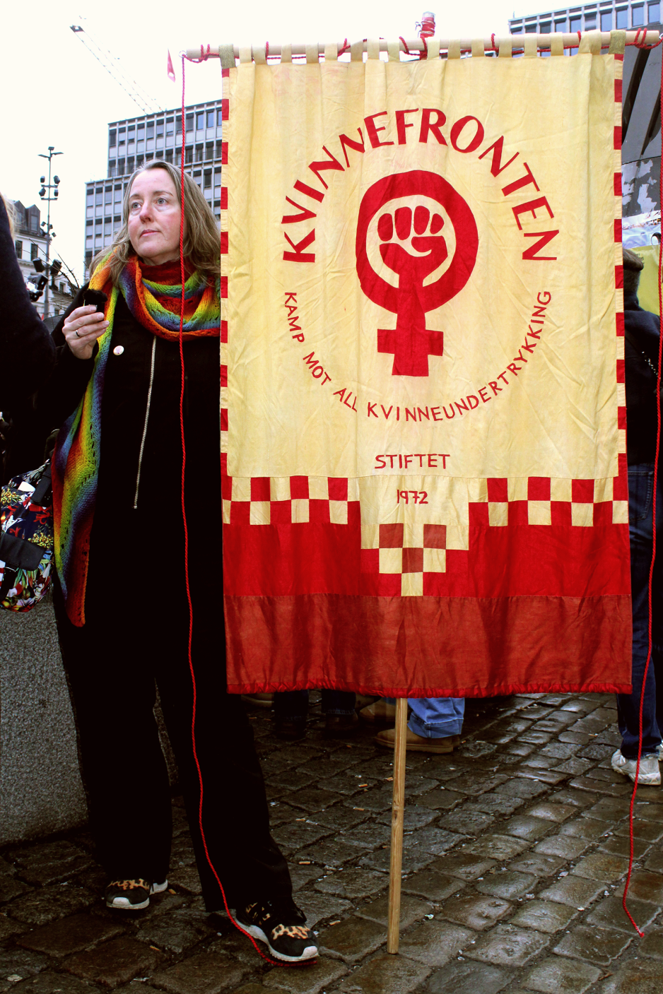 Trude Koksvik Nilsen fra Kvinnefronten står vedsiden av banneret deres. Logoen har et kvinnetegn med en knyttneve, over står teksten kvinnefronten