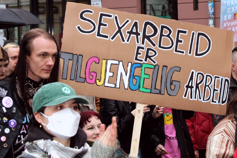 En dame i rullestol løfter et skilt der det står sexarbeid er tilgjengelig arbeid