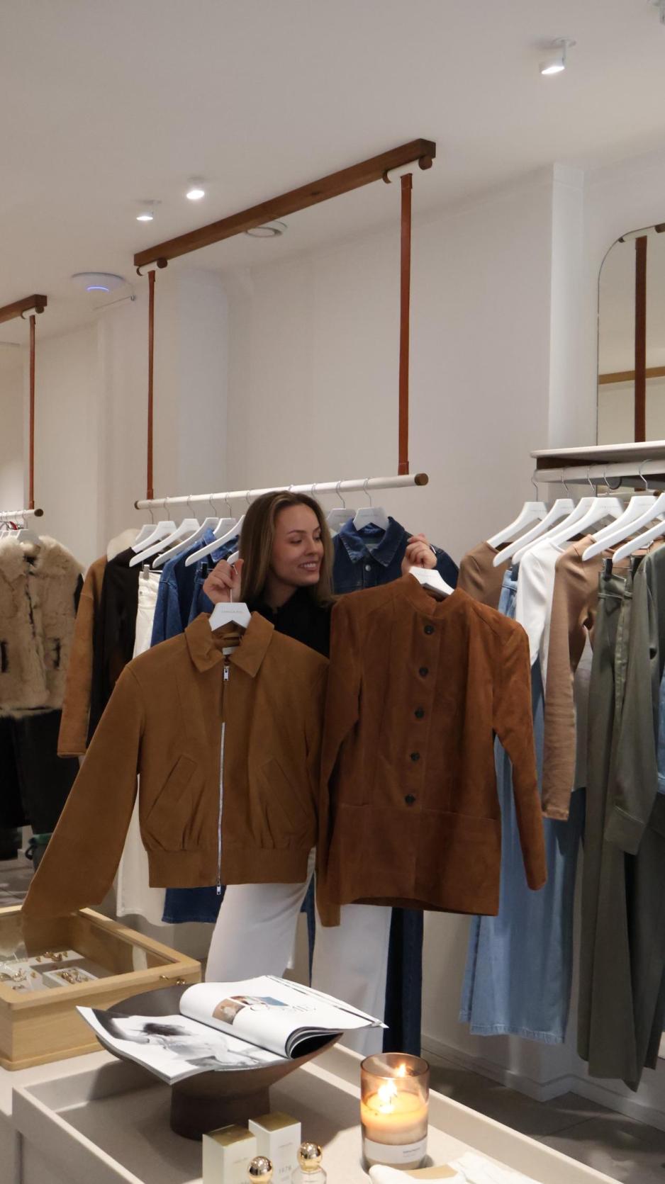 Butikkansatt holder opp to semsket skinn ajkker som hun mener blir vårens største trend