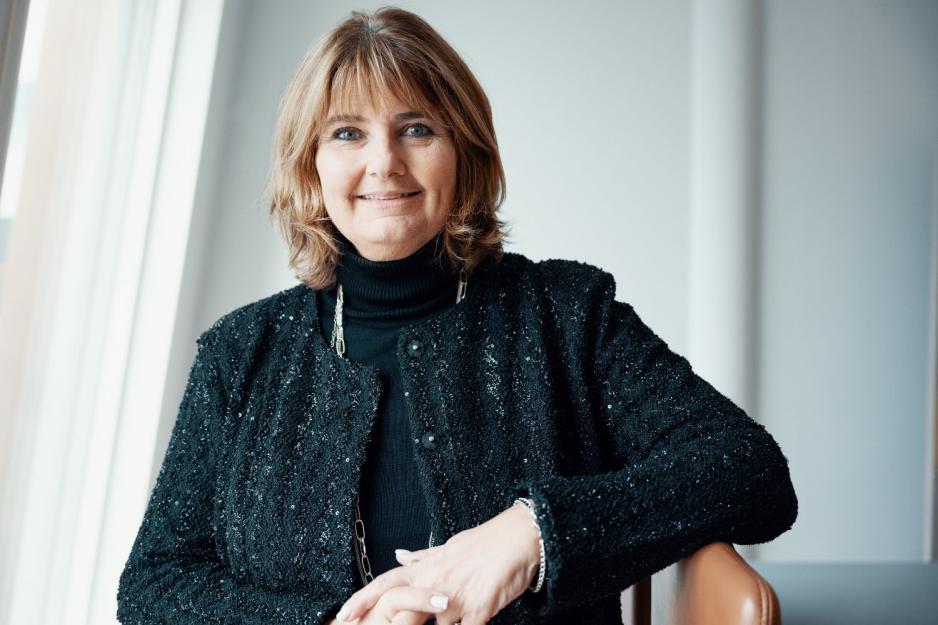 Dame med brunt h&aring;r og sorte kl&aelig;r smiler i kamera. 