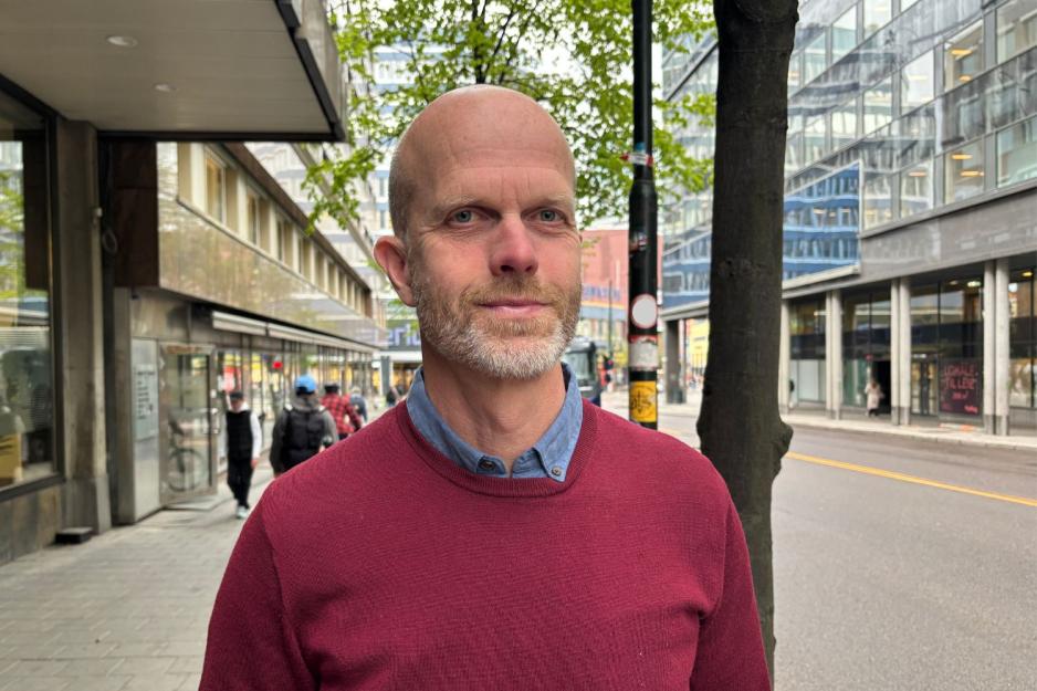 Mann med r&oslash;d genser smiler til kamera ute i gata. 