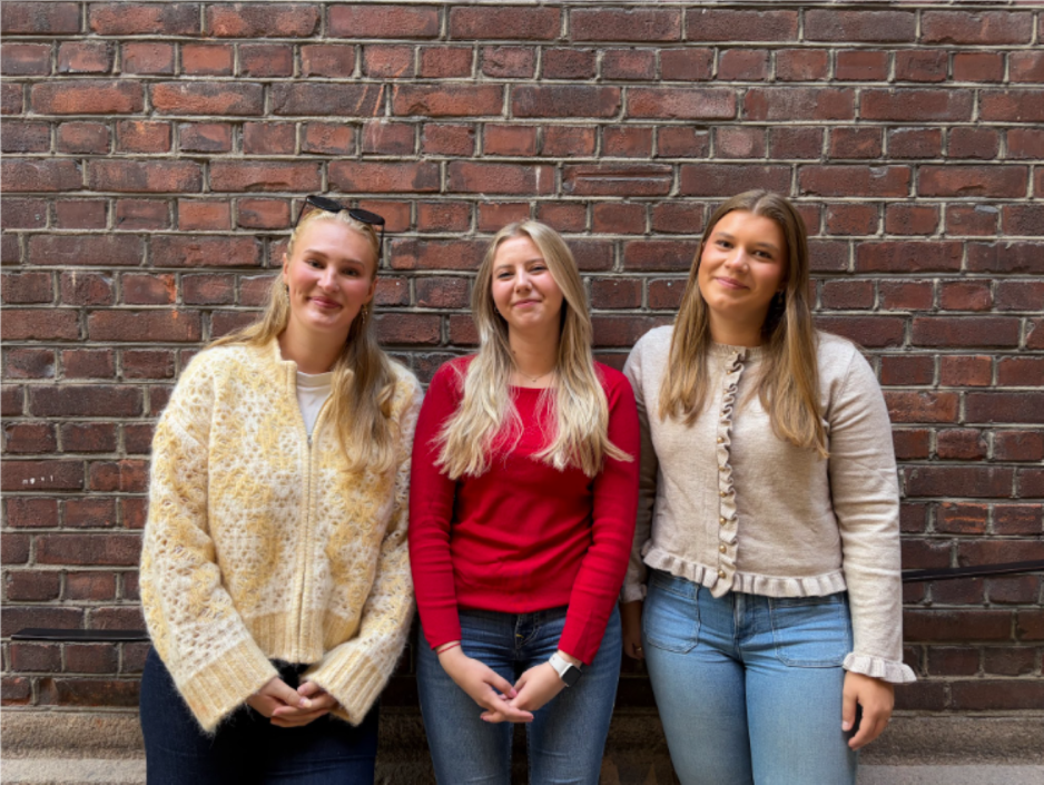 Matilde, Petra og Vilde står foran en murvegg inne på OsloMet