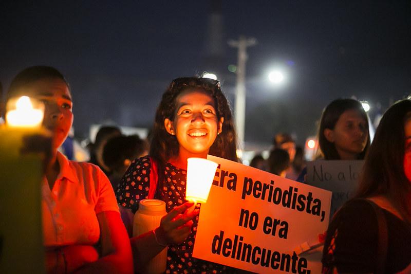 En kvinne smiler mens hun holder opp en plakat med tekst p&aring; spansk: "Han var journalist, han var ingen lovbryter," st&aring;r det.