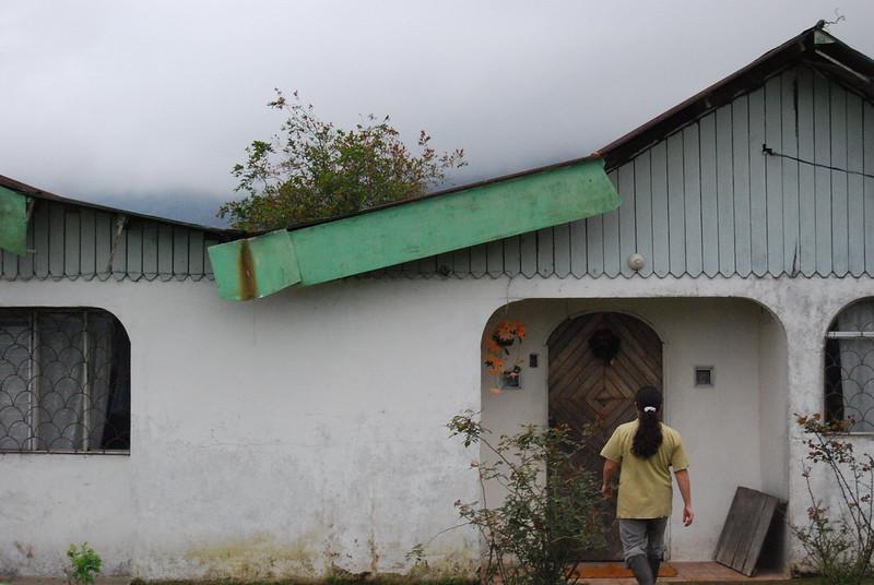 En person g&aring;r mot et hvitt hus i Costa Rica mens tung t&aring;ke henger over hustakene