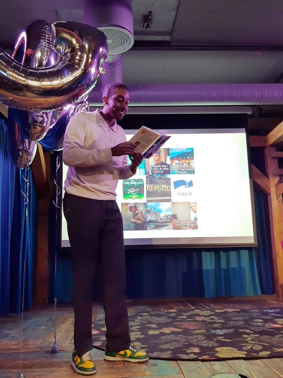 Ahmed Mamow st&aring;r p&aring; kanten av scenen og leser fra en bok.