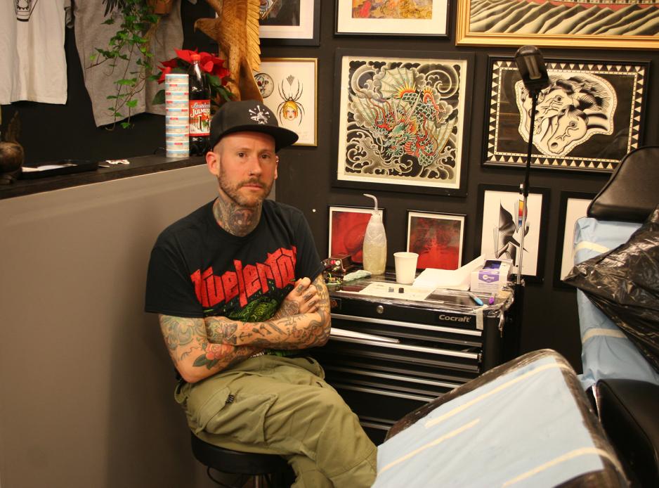 Tatov&oslash;ren sitter p&aring; en krakk, med armene i kors.