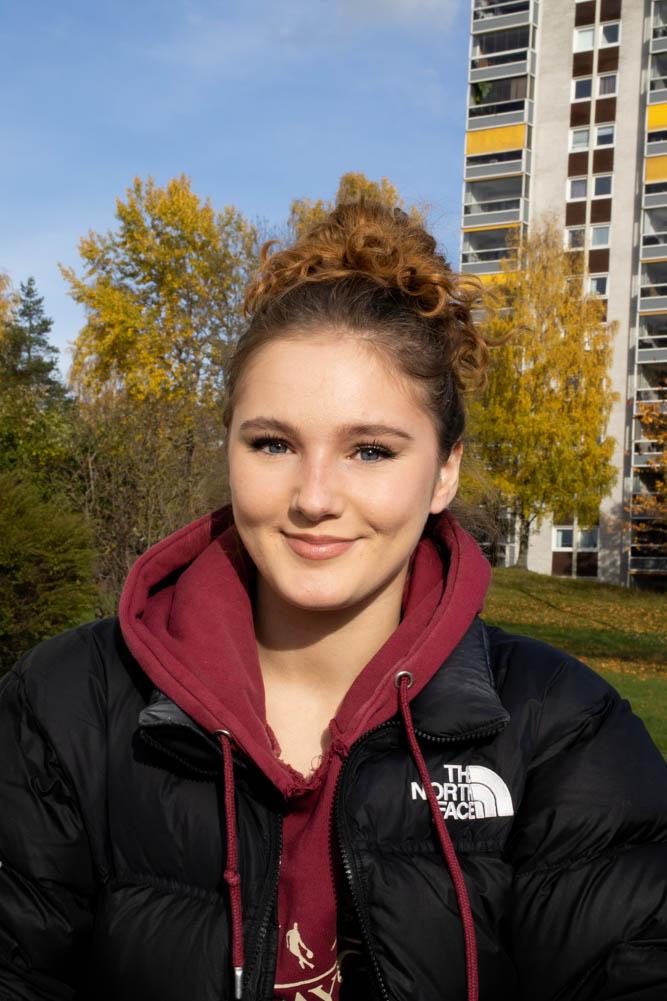 Bildet viser en ung jente med r&oslash;d hettegenser og en svart jakke over. 