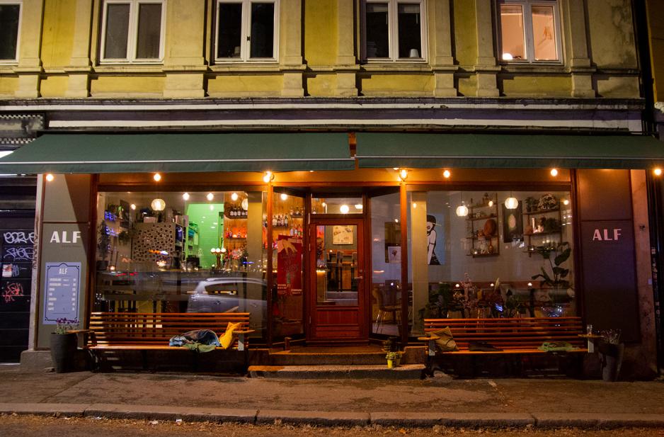 Bildet viser en bar, og litt av gaten foran. Det er ganske m&oslash;rkt, men mange lamper og lykter utenfor. Ved inngangsd&oslash;ren henger en plakat med navnet p&aring; utstillingen. 