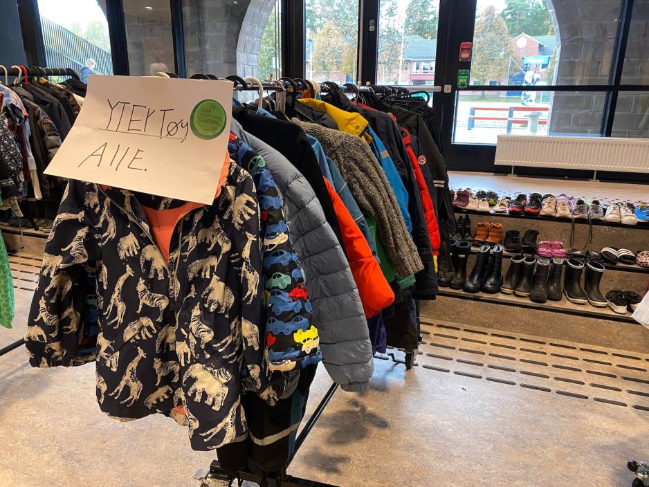 Yttet&oslash;y som henger p&aring; et stativ. Stativet har en lapp p&aring; seg hvor det st&aring;r: yttert&oslash;y alle. I bakgrunnen st&aring;r det mange sko som skal byttes.