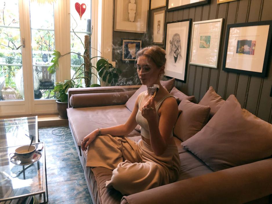 Alma Skolmen sitter i sofaen, og surrer r&oslash;yken rundt kroppen hennes for &aring; rense opp negative energier. 