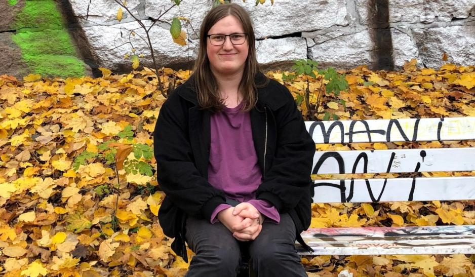 videreg&aring;ende elev sitter p&aring; benk, med gult l&oslash;v p&aring; bakken og i bakgrunnen