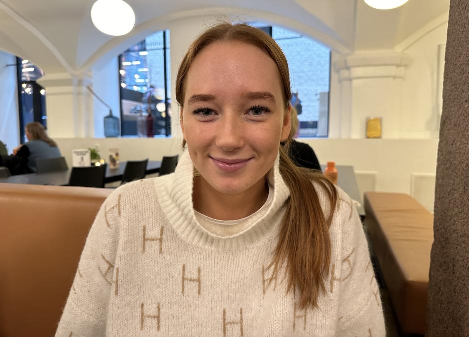 En jente med r&oslash;dt h&aring;r som smiler mot kamera