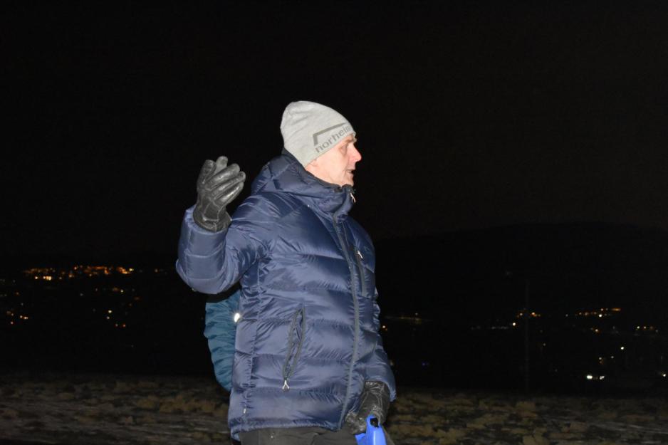 En mann i boblejakke og gr&aring; lue viser noe med en vottekledt h&aring;nd i m&oslash;rket. Han er engasjert. 