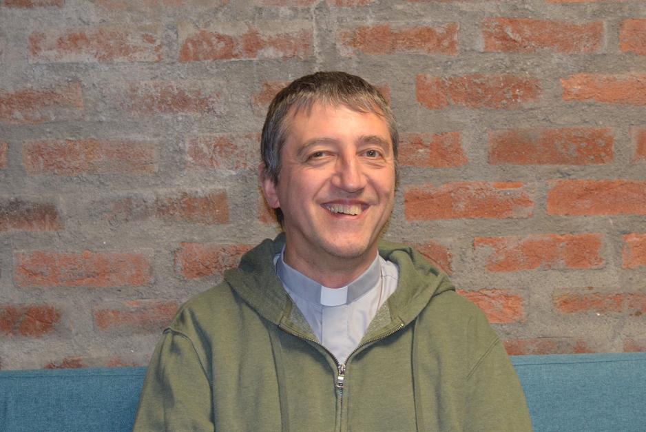 En mann i 50-&aring;rene ser inn i kamera og smiler foran en murvegg.
