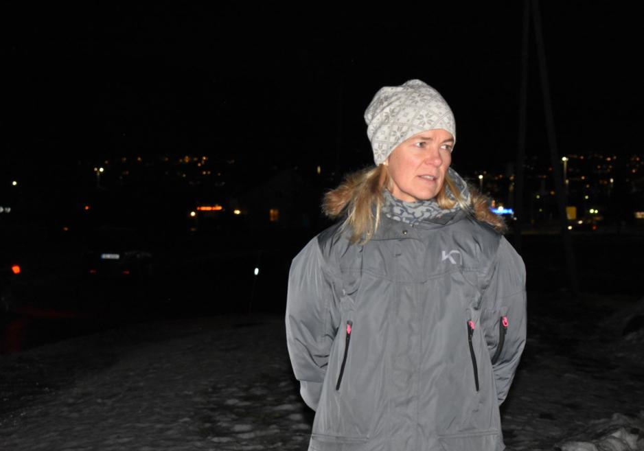 En dame i vinterk&aring;pe og bl&aring; lue st&aring;r i m&oslash;rket og ser alvorlig ut. Hun har blondt h&aring;r halvlangt h&aring;r som stikker ut fra lua.