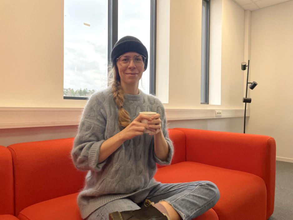 En kvinne sitter med en kaffekopp i sofaen p&aring; biblioteket