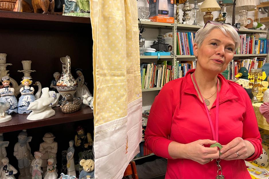 Eldre dame med rosa skjorte st&aring;r ved siden av en hylle med figurer.