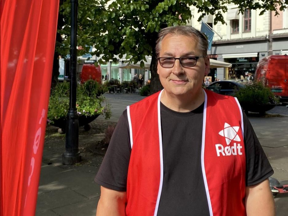 Atle Wilhelmsen st&aring;r i Karl Johan, ved siden av et flagg fra R&oslash;dt og smiler til kameraet.