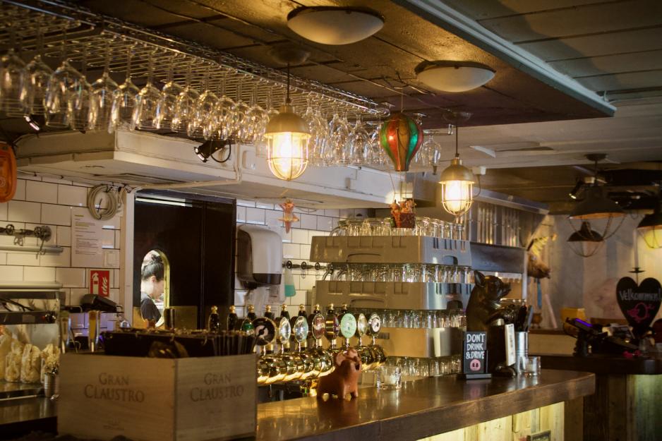 Baren hos den Glade Gris. Man ser en dame gjennom et vindu til kj&oslash;kkenet.