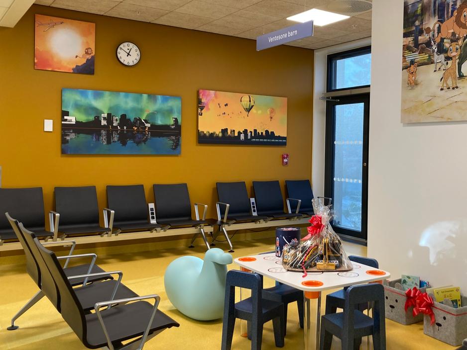Venterom for barn p&aring; legevakten, med gulbrun vegg, fargerike bilder p&aring; veggene, stolrader og leker. 