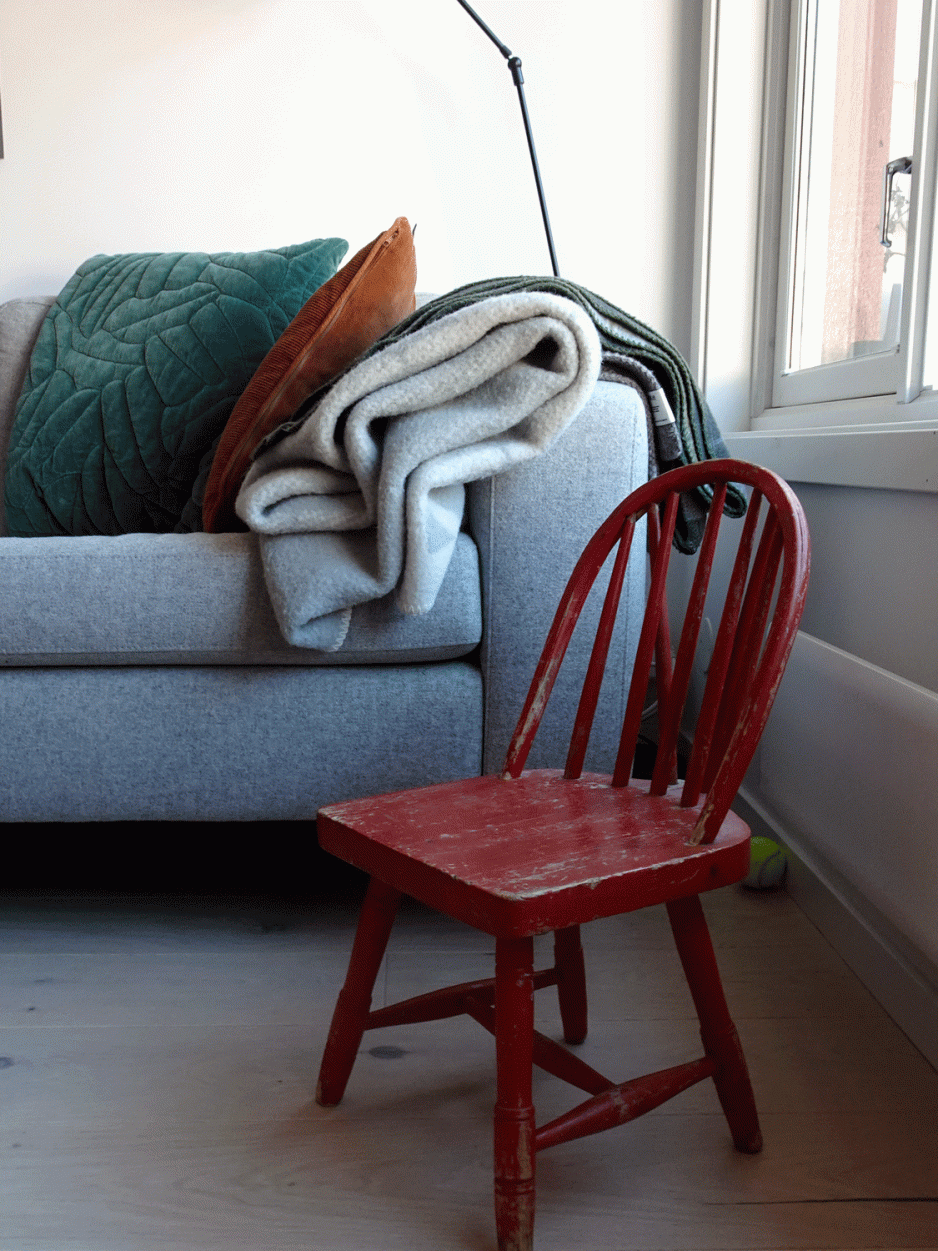 Raud og slitt barnestol foran ein gr&aring; sofa.