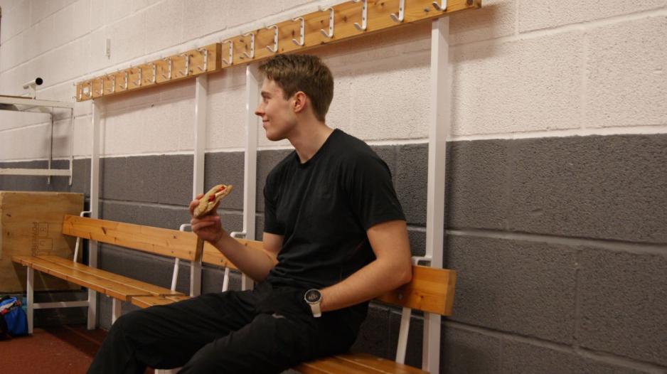 Benjamin sitter p&aring; en benk og spiser et rundstykke.