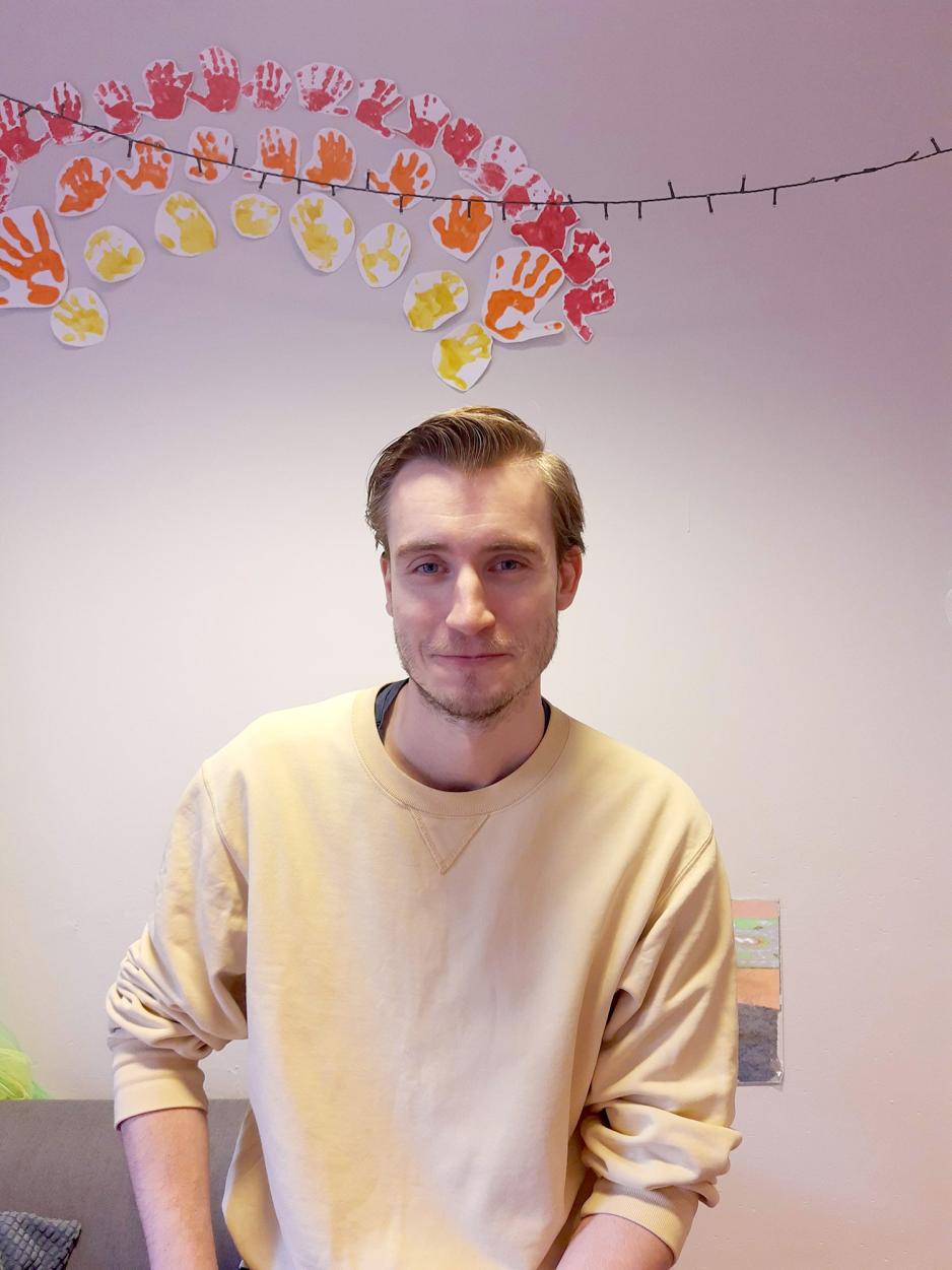 Mann foran en vegg med en regnbue laget av malte hender.