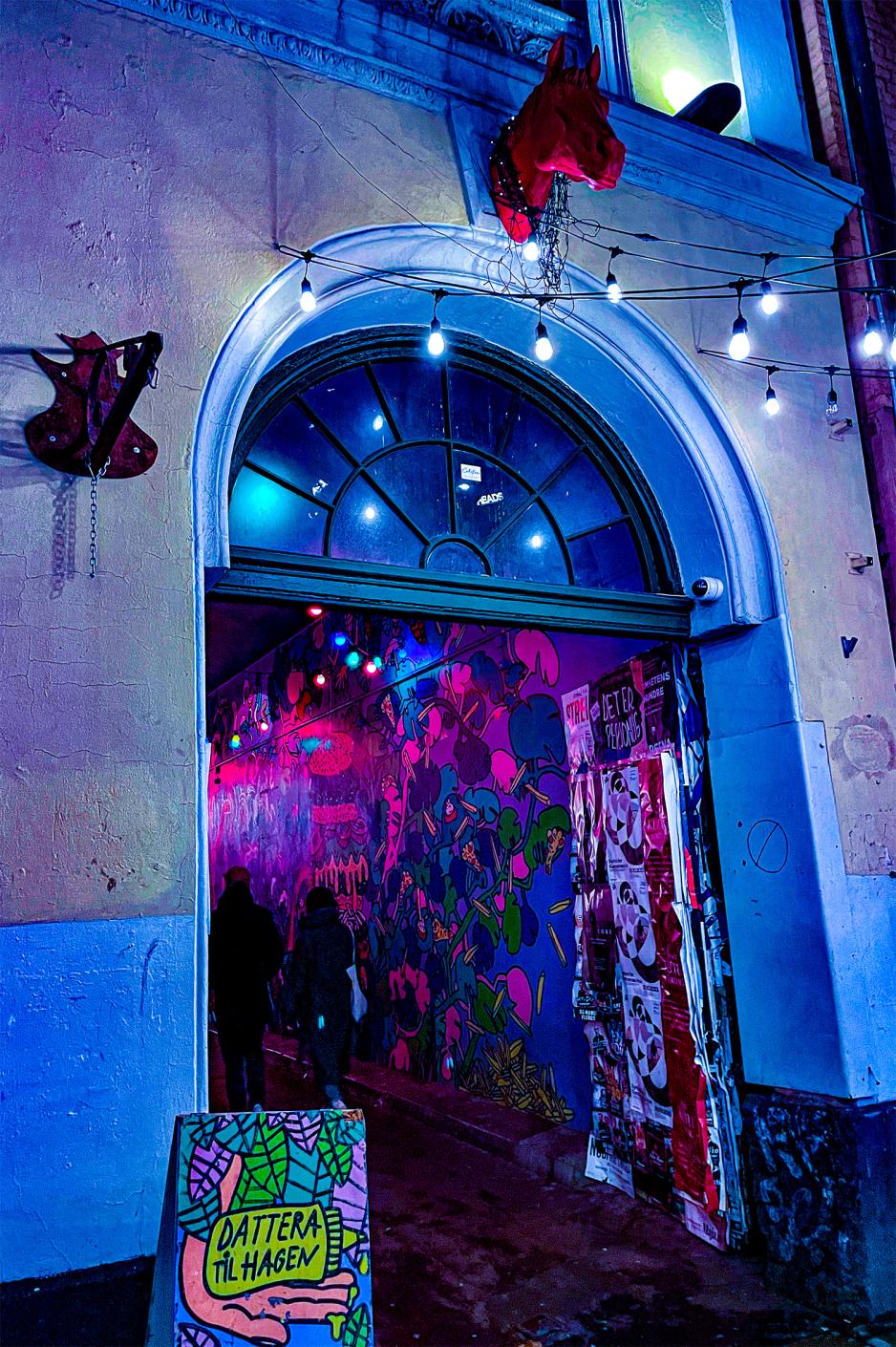 Buet inngang til hus. Et fargerikt skilt st&aring;r foran inngangen. Et hestehode i r&oslash;d plast henger over inngangen. Det er masse forskjellige farver p&aring; veggene. 