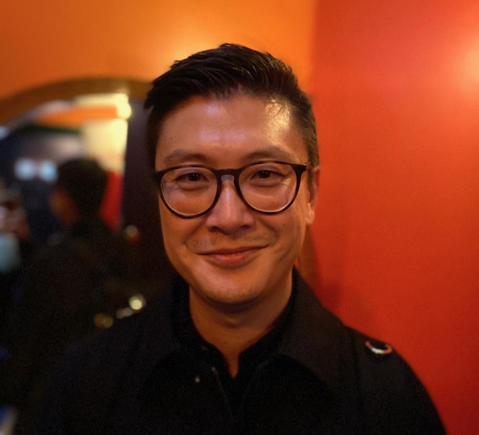 Bildet viser et portrettbilde av Derek Bj&oslash;lgerud. Han smiler til kameraet. Han har p&aring; seg sorte briller, og sorte kl&aelig;r. H&aring;ret er ogs&aring; m&oslash;rkt.