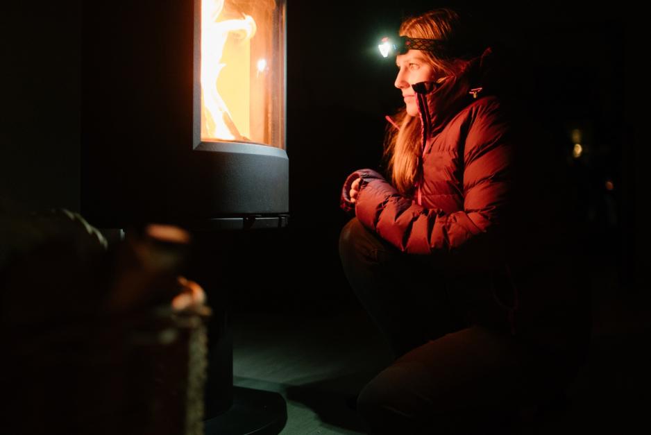 En kvinne sitter foran en vedovn for &aring; holde varmen