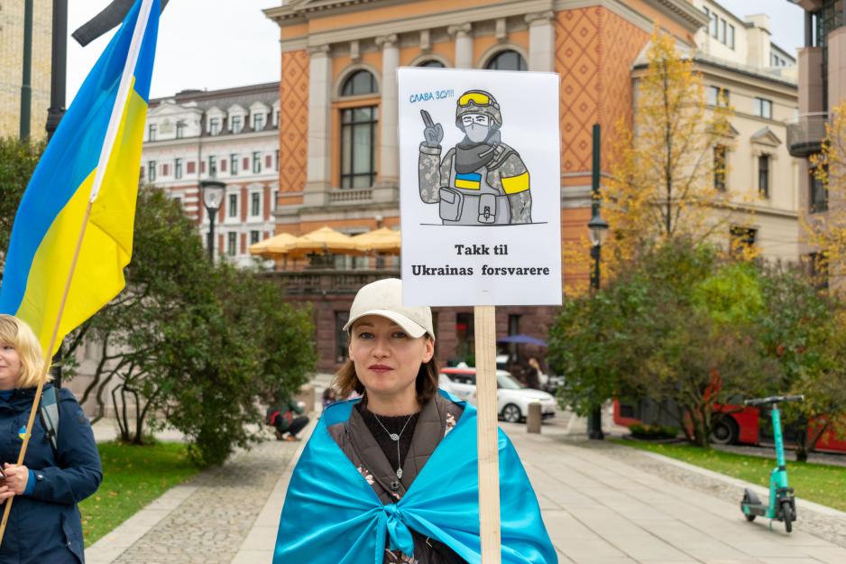 Kvinne med det ukrainske flagget rundt seg og en plakat der det st&aring;r takk til Ukrainas forsvarere