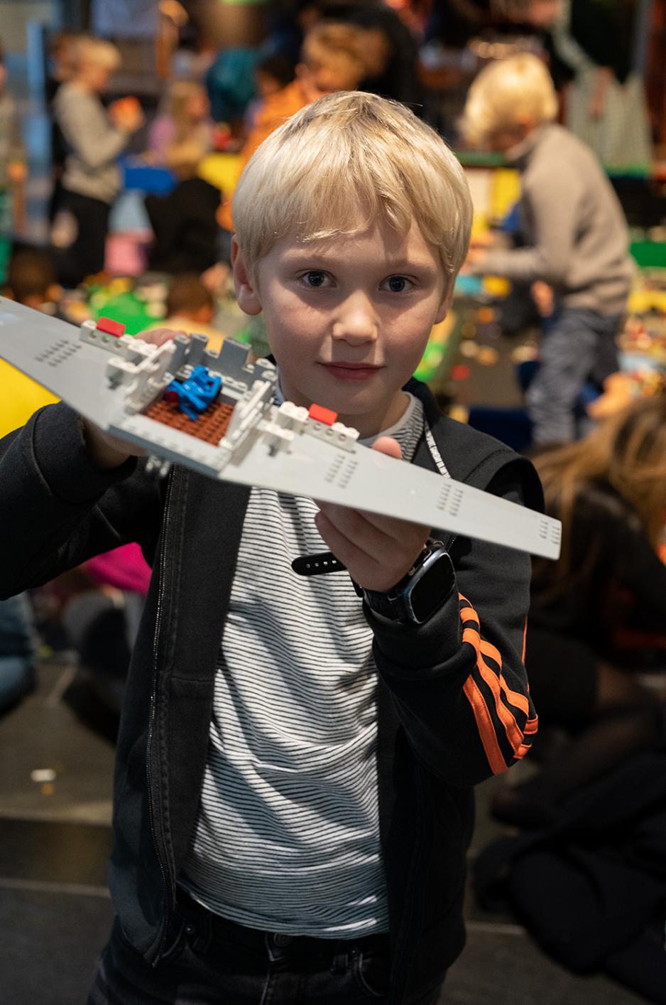 En lysh&aring;ret gutt holder opp et gr&aring;tt legofly