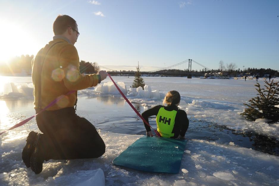 En av l&aelig;rerne hjelper en elev &aring; g&aring; uti isvannet.