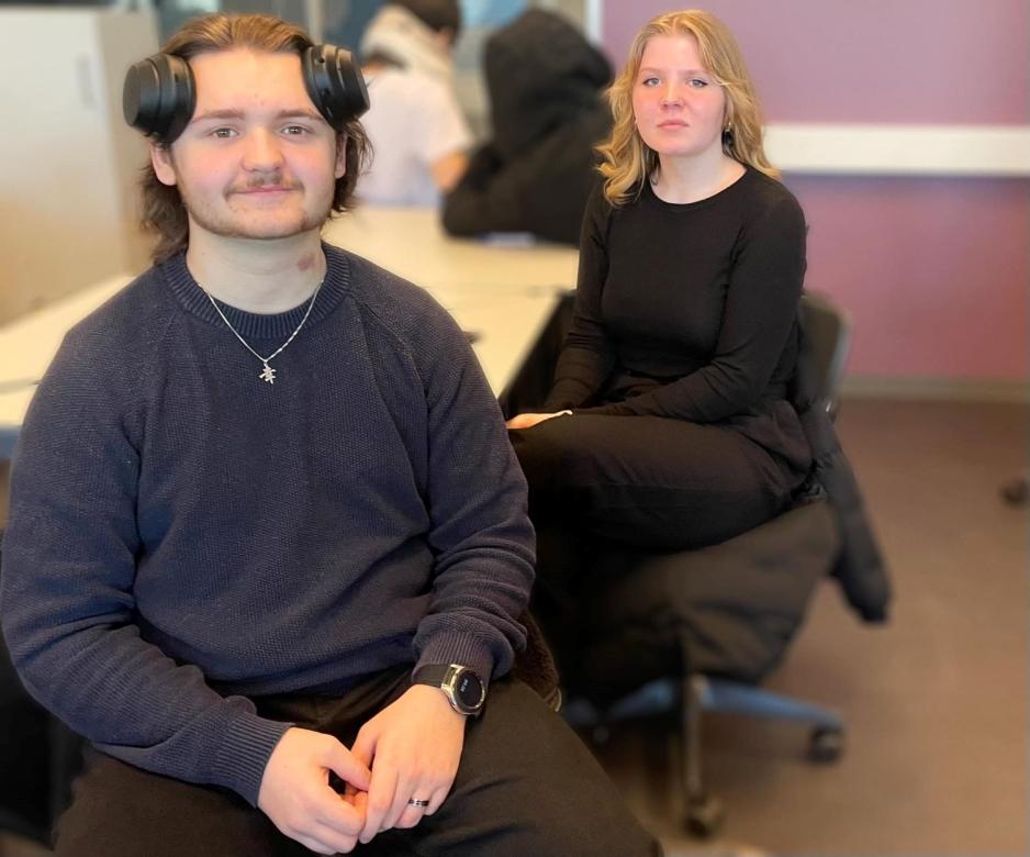 En gutt og en jente sittende p&aring; hver sin stol. Gutten har p&aring; seg svarte kl&aelig;r og har hodetelefoner p&aring; &oslash;rene. Malin er blond, har p&aring; seg svarte kl&aelig;r.