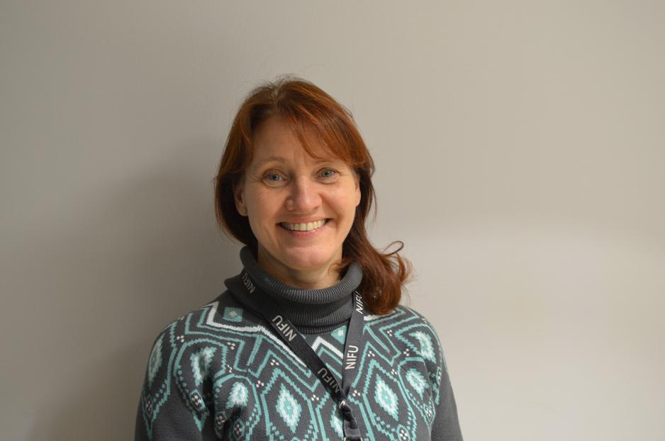 Kvinne smiler i strikkagensere p&aring; n&aelig;rt hold.