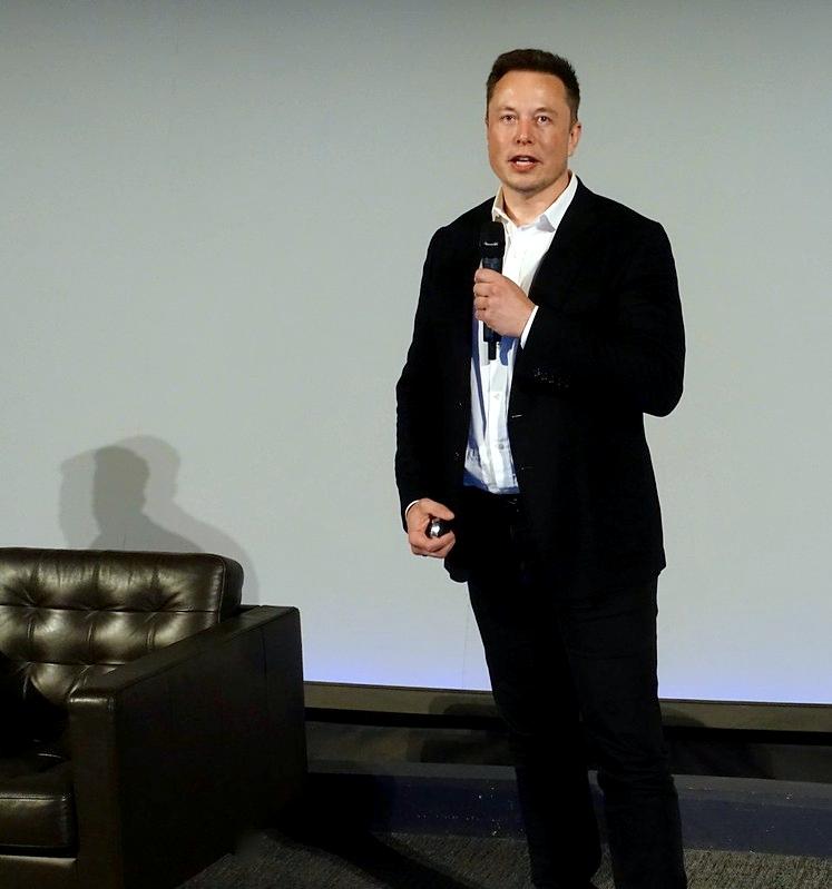 Elon Musk st&aring;r i dress og snakker i en mikrofon.