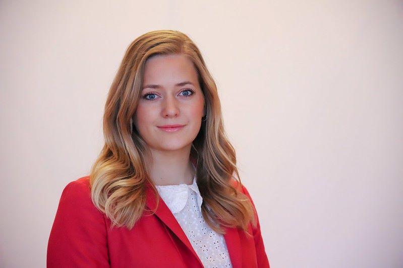 Bilde av kvinne med blondt h&aring;r og r&oslash;d dressjakke. 