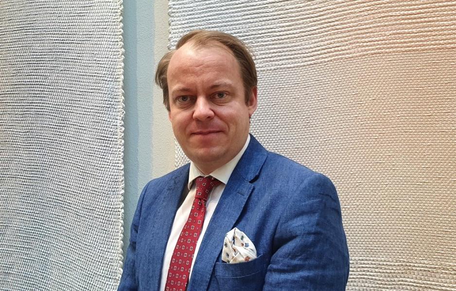 Erlend Wiborg ser mot kameraet, ikledd bl&aring; dress og r&oslash;dt slips. 