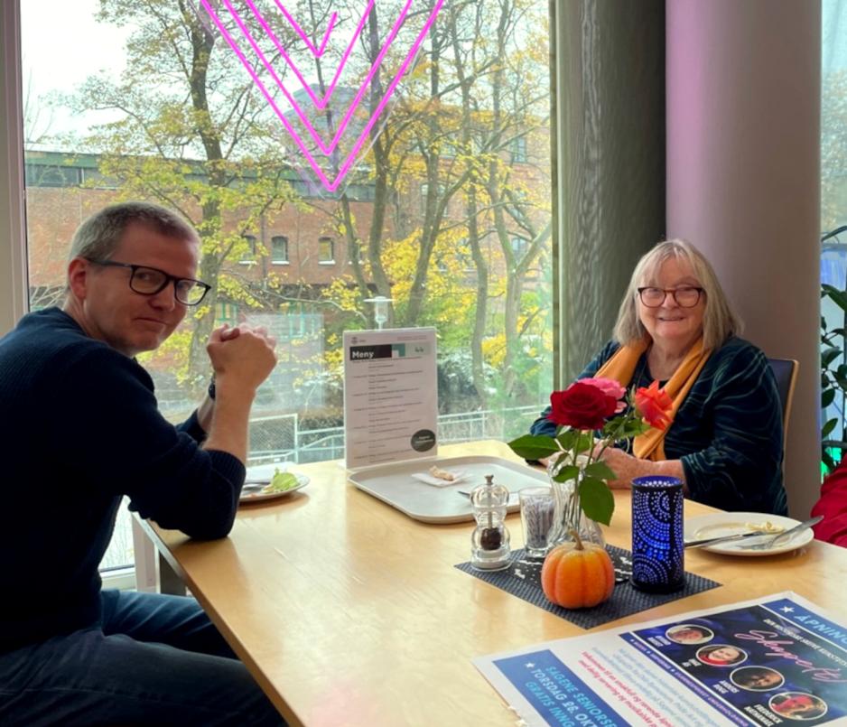 En mann og en dame sitter ved et bord. En rosa trekant er p&aring; vinduet.