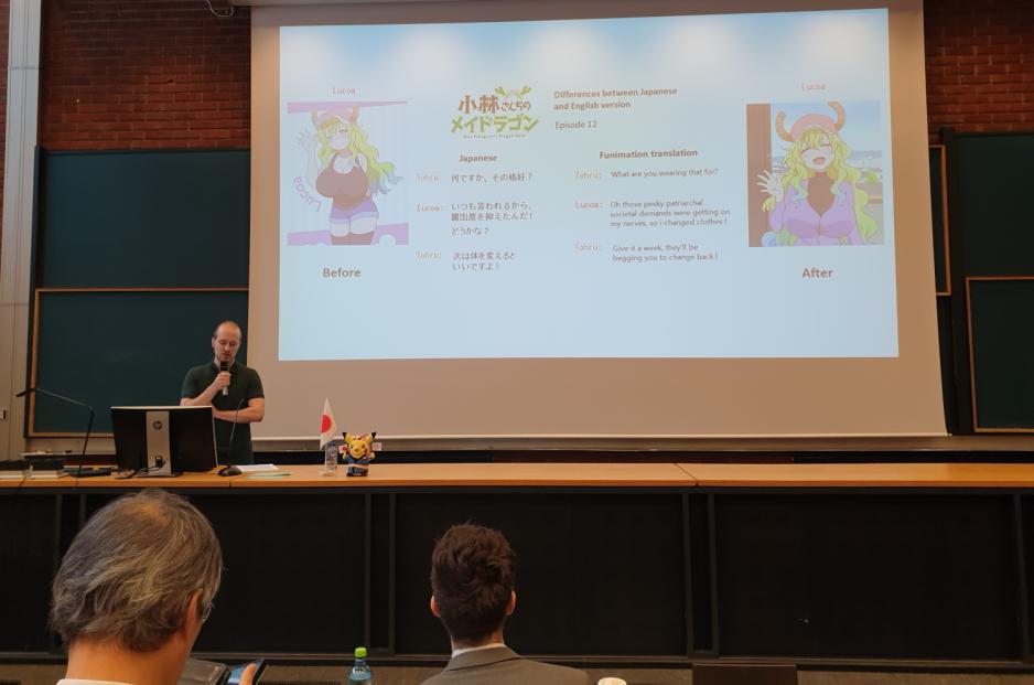 Mann st&aring;r p&aring; et podie og taler foran en power point med bilde av en anime jente