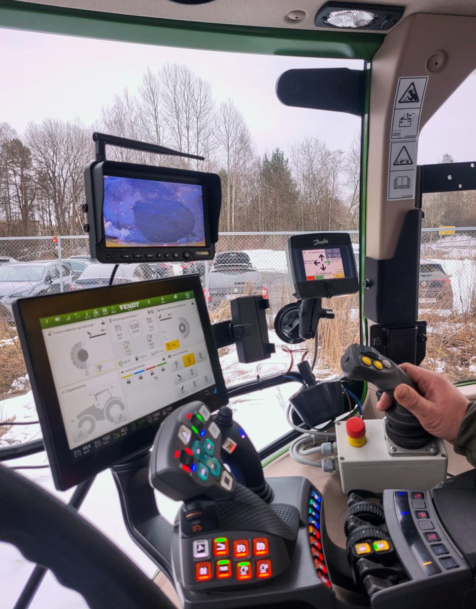 Bilde av f&oslash;rerhuset inne i feietraktoren, sj&aring;f&oslash;ren har h&aring;nden p&aring; en av spakene og man kan se mange knapper og spaker og skjermer