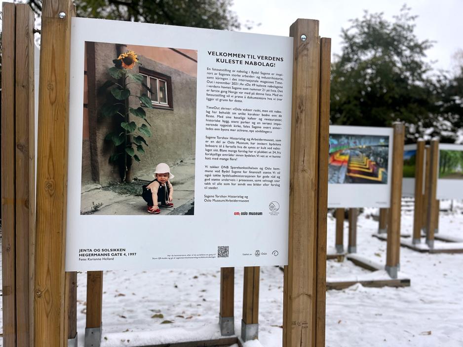 Bildet er viser en fotoutstilling. Man ser et bilde s&aelig;rlig godt av en liten jente med en solsikke i bakgrunnen. Rundt om utstillingen er det sn&oslash;. 